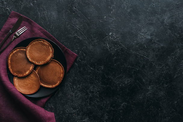 top view of plate of chocolate pancakes on black surface - Φωτογραφία, εικόνα
