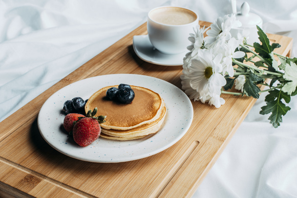 Ontbijt op bed met pannenkoeken en koffie op houten dienblad - Foto, afbeelding