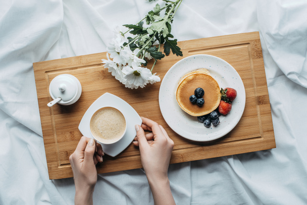 cropped shot of woman eating breakfast with pancakes and coffee in bed - Foto, Imagem