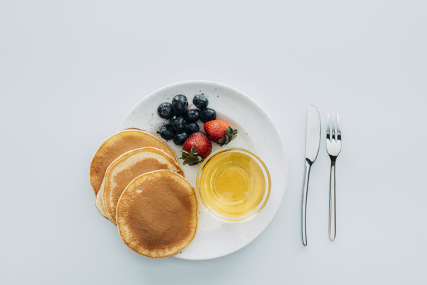 bovenaanzicht van pannenkoeken met bessen en maple siroop op witte tafel - Foto, afbeelding