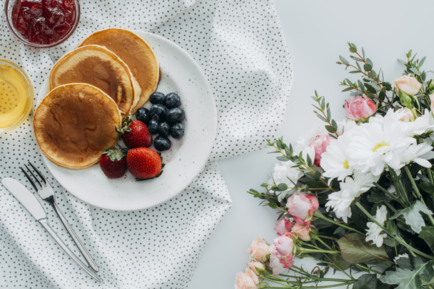 top view of tasty breakfast with pancakes and flowers bouquet on white - Photo, Image