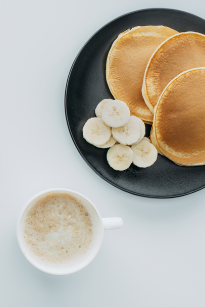 top view of pancakes with sliced banana and cup of coffee on white table - Foto, immagini