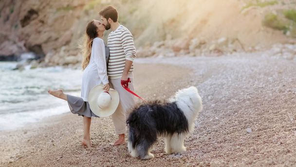 Junge Paare stehen mit flauschigem Hund am Strand und küssen sich - Foto, Bild