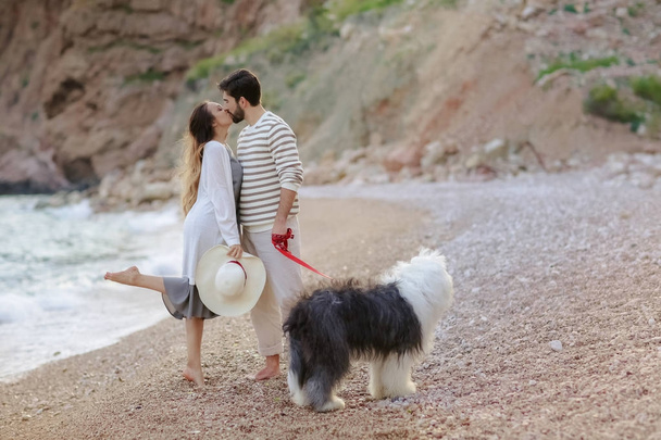 full length of young couple standing with fluffy dog on beach and kissing - Photo, image