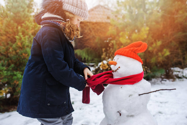 happy kid girl making snow man on Christmas vacations on backyard. Winter outdoor activities for kids. - Foto, Imagen