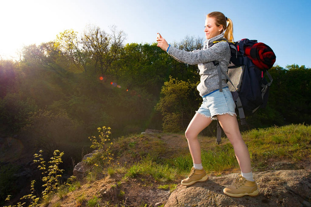 Een meisje met rugzak, het nemen van de foto van het mooie landschap met mobiele telefoon in een wandeling in het bos. Reizen, vakantie, vakantie en avontuur concept. Bos landschap-achtergrond - Foto, afbeelding