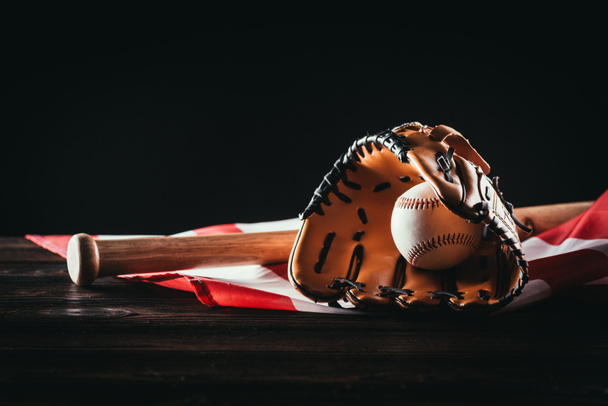 крупним планом вигляд бейсбольної рукавички з м'ячем і кажаном на дерев'яному столі і прапором США на чорному
 - Фото, зображення