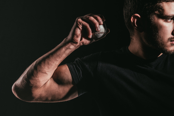 Schnappschuss eines jungen muskulösen Sportlers mit Baseballball isoliert auf schwarz - Foto, Bild
