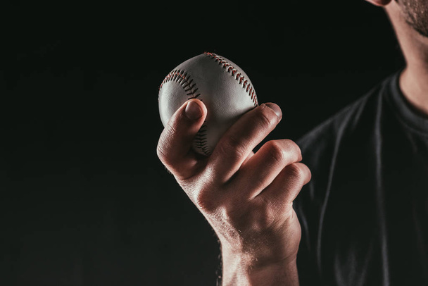 cropped shot of young sportsman holding baseball ball isolated on black - Fotoğraf, Görsel
