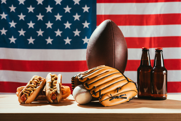 bierflessen met hotdogs en sportuitrusting met Amerikaanse vlag achter   - Foto, afbeelding