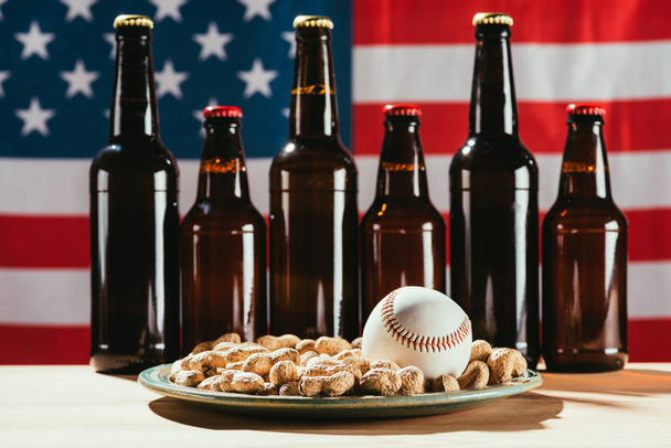 close-up view of baseball ball on plate with peanuts and beer bottles with american flag behind - 写真・画像