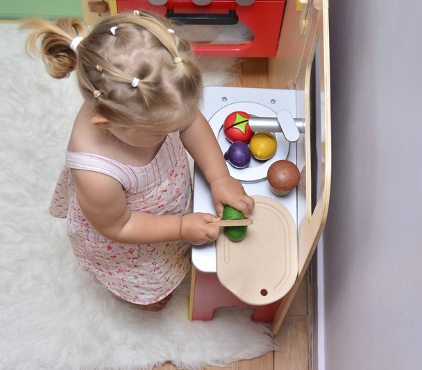 girl cuts wooden vegetables on toy kitchen - Фото, изображение