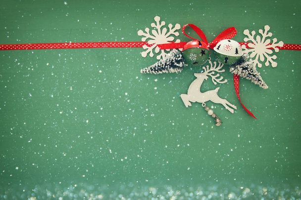 Christmas background with red silk traditional ribbon, white deer, evergreen tree, paper snowflakes and jingle bells. - Photo, Image