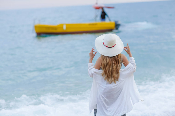 uzun kıvırcık saç ayakta görünümü tekne deniz geri Yüzme bakarak sahilde olan kadın - Fotoğraf, Görsel