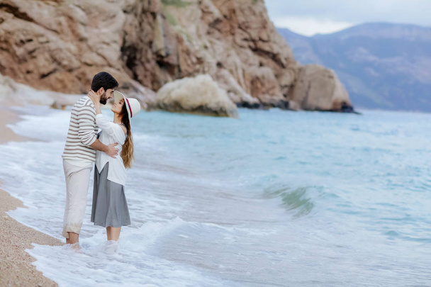 stylish young couple in love hugging standing on beach barefoot with cliff and mountain on background, full length - Foto, Bild