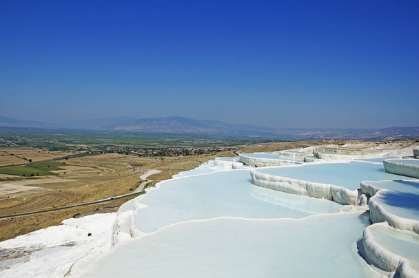  De warmwaterbron van Pamukale stijgt boven de omringende velden en steppen op een warme, hete dag. Kalksteen stroomgebieden van Pamukale in Turkije. - Foto, afbeelding