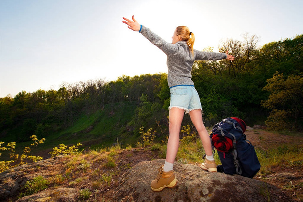 Jonge vrouw met handen omhoog staande op de top van de berg genieten van de mooie dag. Reizen, vakantie, vakantie en avontuur concept. Bos landschap-achtergrond - Foto, afbeelding