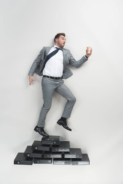 overhead view of businessman with coffee to go in hand standing on pile of folders isolated on grey - Foto, Imagem