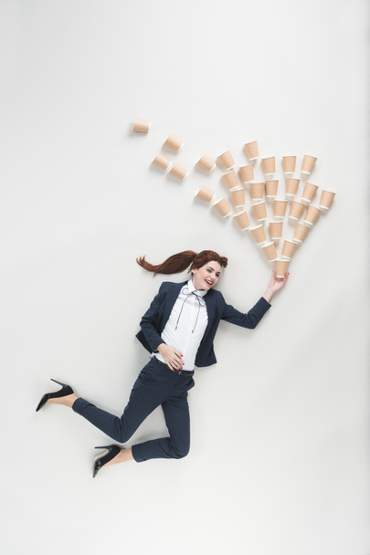 overhead view of cheerful businesswoman with disposable cups isolated on grey - Photo, Image