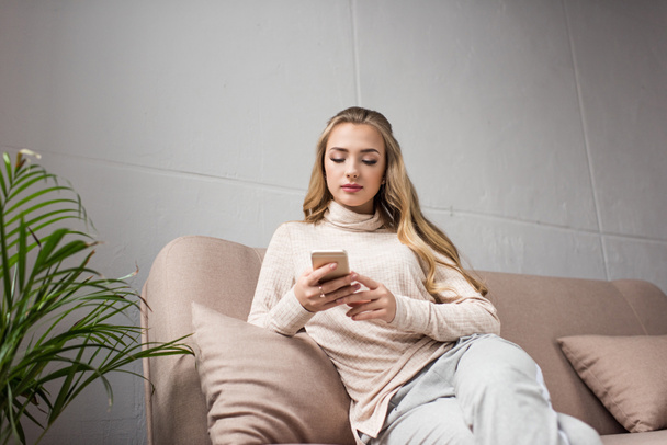 relaxado jovem mulher usando smartphone no sofá em casa
 - Foto, Imagem