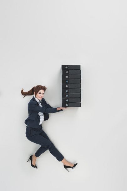 overhead view of smiling businesswoman holding pile of folders isolated on grey - Foto, imagen