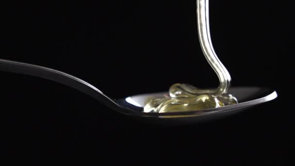 miel goteando de la cuchara de té inoxidable sobre fondo negro
 - Metraje, vídeo
