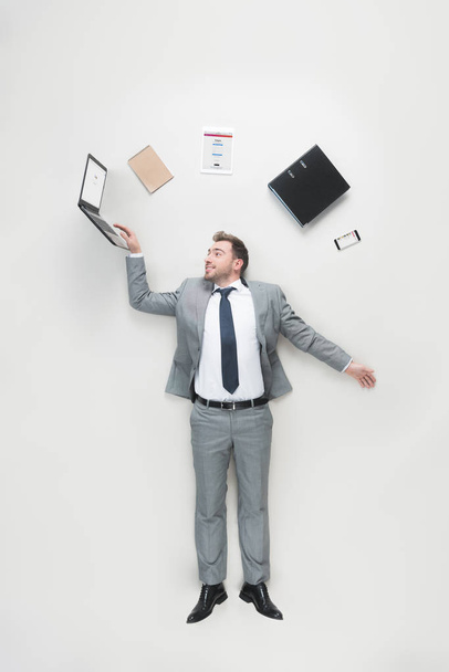 overhead view of businessman with office supplies above head using laptop isolated on grey - 写真・画像
