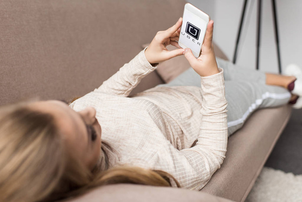 woman on couch using smartphone with uber logo on screen - Foto, Imagen