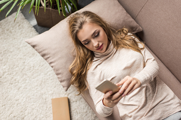 high angle view of young woman using smartphone on couch at home - Фото, зображення