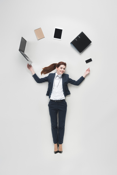 bovenaanzicht van zakenvrouw met diverse kantoorbenodigdheden met behulp van laptop geïsoleerd op grijs - Foto, afbeelding
