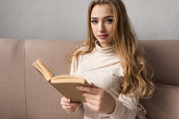 attractive young woman reading book on couch - Zdjęcie, obraz