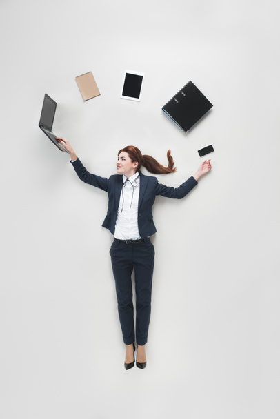 overhead view of businesswoman with various office supplies using laptop isolated on grey - Foto, imagen