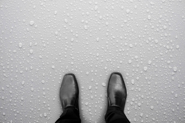 Бізнесмен в чорному взутті, що стоїть на білій мокрій підлозі. Вода падає на підлогу. Обережно, слизька підлога
. - Фото, зображення