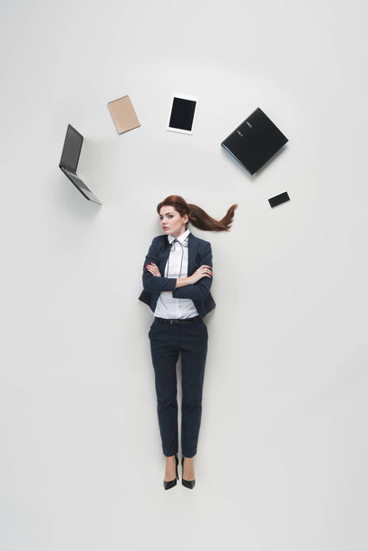 overhead view of businesswoman with various office supplies above head isolated on grey - Photo, Image