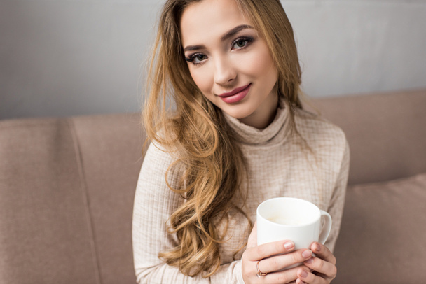 close-up portrait of young woman drinking coffee on couch at home - Foto, Imagen