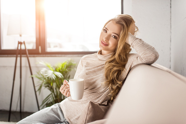 beautiful young woman drinking coffee on couch at home - Foto, Imagem
