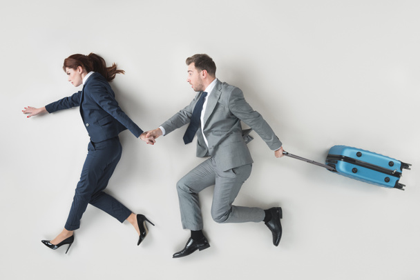overhead view of business coworkers with suitcase holding hands isolated on grey - Foto, afbeelding