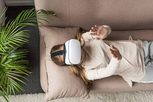 pohled z vysokého úhlu mladé ženy v soupravu pro virtuální realitu ležet na gauči - Fotografie, Obrázek