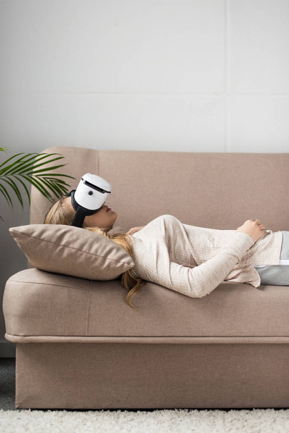 vista lateral de la mujer joven en auriculares de realidad virtual tumbado en el sofá
 - Foto, imagen