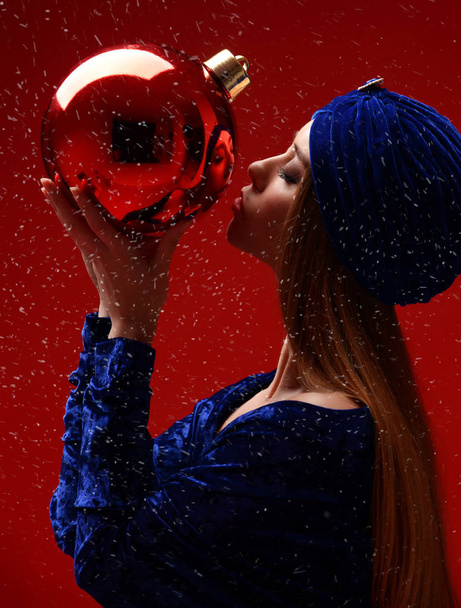 Portrait of young beautiful fashion woman in blue stylish winter dress and hat kissing bug christmas decoration ball  - Photo, Image