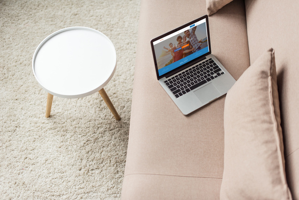 υψηλή γωνία άποψη του lap-top στέκεται στον άνετο καναπέ με couchsurfing ιστοσελίδα στην οθόνη - Φωτογραφία, εικόνα