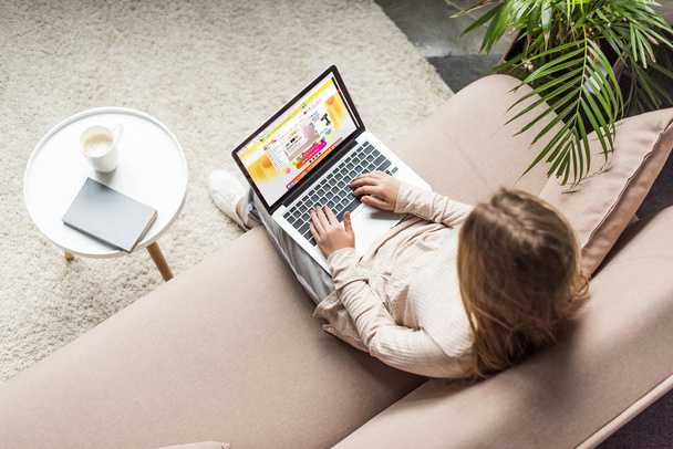 high angle view of woman at home sitting on couch and using laptop with aliexpress website on screen - Foto, Bild