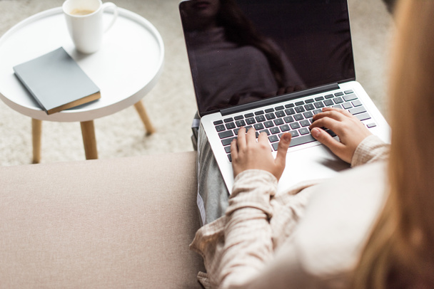 обрезанный снимок молодой женщины, работающей с ноутбуком на диване
 - Фото, изображение
