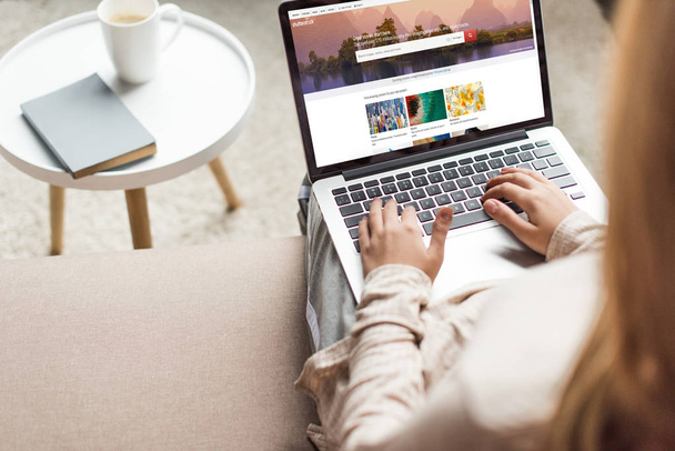 cropped shot of woman at home sitting on couch and using laptop with shutterstock website on screen - Photo, Image