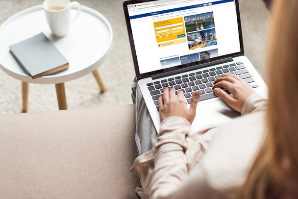 cropped shot of woman at home sitting on couch and using laptop with booking website on screen - Fotografie, Obrázek