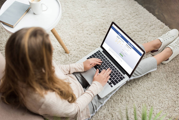 high angle view of woman at home sitting on floor and using laptop with facebook website on screen - Foto, Imagem