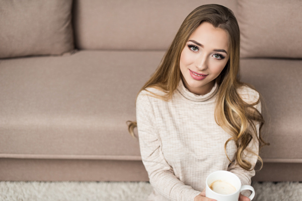 smiling young woman in warm sweater with cup of hot drink at home - Фото, зображення