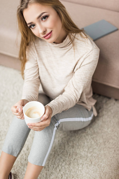magas, szög, kilátás a gyönyörű fiatal nő ül a padlóra csésze kávé - Fotó, kép