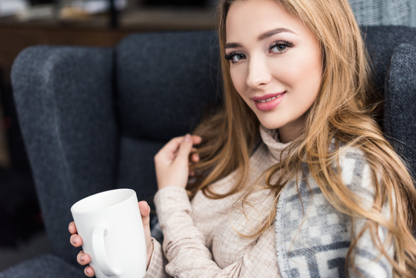 beautiful young woman sitting in comfy armchair with cup of coffee - Photo, Image