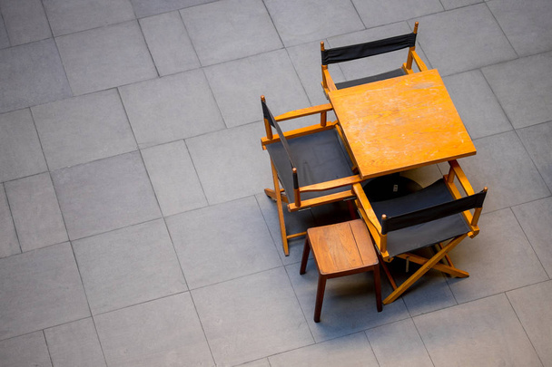 Έπιπλα εξωτερικού χώρου που περιλαμβάνουν ξύλινο τραπέζι και καρέκλες στο πάτωμα σκούρο κεραμικών κεραμιδιών. Εξωτερική διακόσμηση σχεδιασμός. - Φωτογραφία, εικόνα